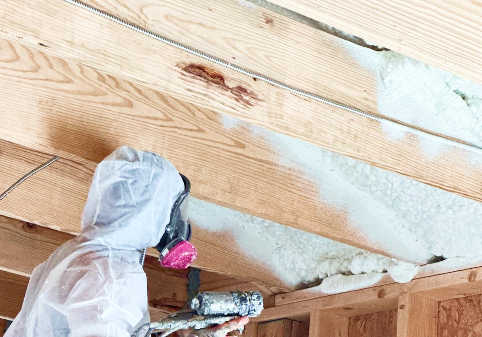 Installer applying spray foam between timber roof rafters