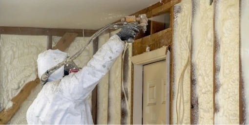 Installer spraying foam insulation into wall framing
